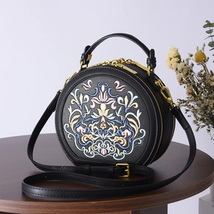 Detailed close-up of intricate floral embroidery on black leather round crossbody bag
