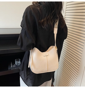Close-up of white leather bucket bag with embroidered strap and fashion trend label
