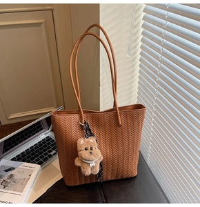 Brown woven tote bag with shoulder strap and plush bear charm in office setting