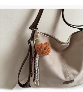 Detailansicht eines braunen Plüschbären-Anhängers mit Kordel an einer beigen Wildledertasche