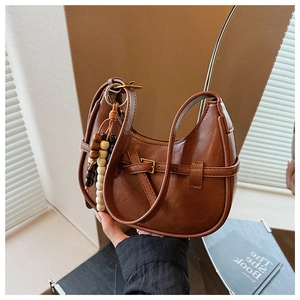 Detail of caramel crescent crossbody bag with decorative strap and colorful bead pendant