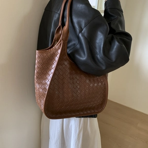 Detailed view of brown woven tote bag on shoulder showing intricate intrecciato texture