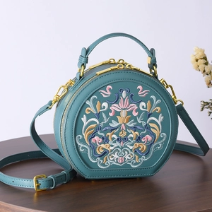 Close-up of floral embroidery on a vintage dark green round bag with golden hardware