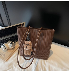 Detail of a brown woven tote bag with a plush bear charm and pearl accessory