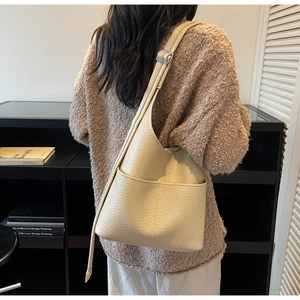 Close-up of cream white bucket bag with lychee texture and adjustable strap on model