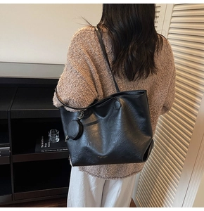 Detail of a large black leather tote bag with a matching round coin purse on a model