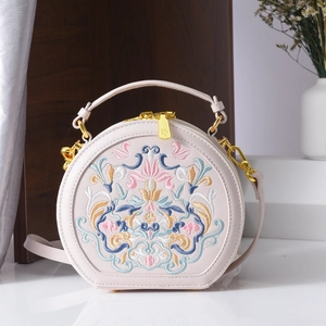 Close-up of vintage floral embroidery and golden zipper on light pink round bag