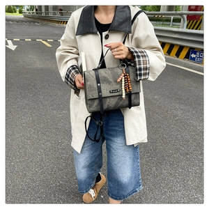Gros plan sur un sac messager gris vintage avec breloque en bois et rivets métalliques