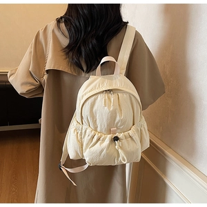 Rear view of a model wearing the cream white pleated nylon backpack in a minimalist room