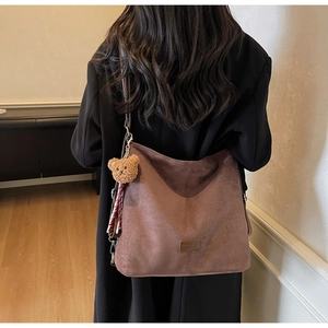 Detail einer großen braunen Wildleder-Hobo-Tasche mit verstellbarem Gurt und Bärenanhänger