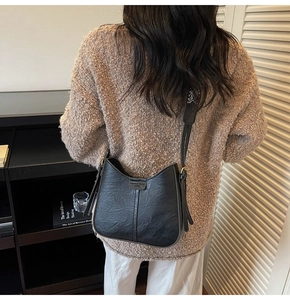 Détail d'un sac hobo en cuir noir avec boucle en métal porté par un mannequin chez soi