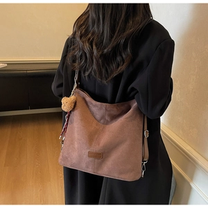 Detail einer braunen Wildledertasche mit Leder-Logo-Patch und niedlichem Bären-Anhänger