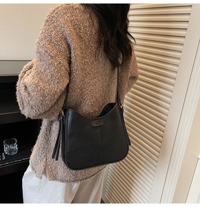 Détail d'un sac Hobo en cuir noir avec logo embossé porté par un mannequin