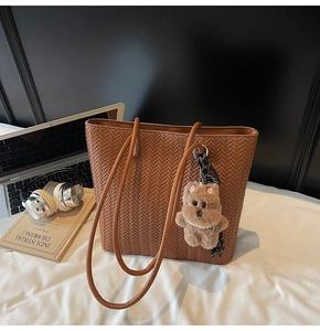 Brown woven tote bag with cute teddy bear charm next to a laptop and books