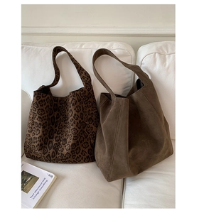 Detail view of large leopard print and solid brown suede tote bags on a white sofa