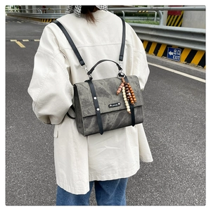 Gros plan d'un sac à dos vintage en cuir gris avec sangles noires et breloque en perles