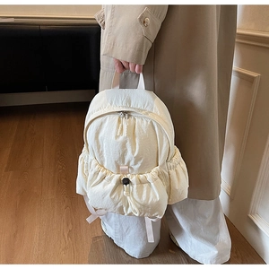 Detail of a cream nylon backpack featuring a drawstring pleated front pocket and metal zippers
