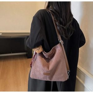 Braune Wildleder-Hobo-Tasche mit Bärenanhänger und Schleife, getragen an der Schulter