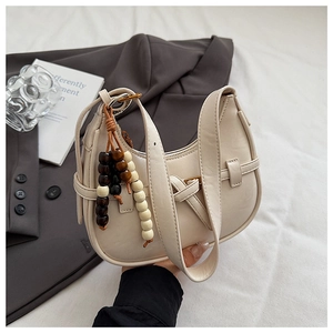 Detail of minimalist cream leather crescent bag with wooden bead tassel and matte texture