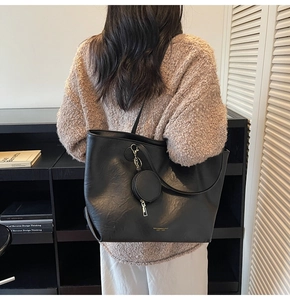 Close-up of black leather tote bag with gold lettering and round coin purse charm