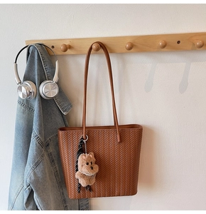 Brown woven tote bag with cute plush bear charm hanging on a minimal wooden rack