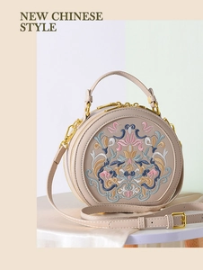 Detail of elegant floral embroidery on a beige round crossbody bag with golden hardware