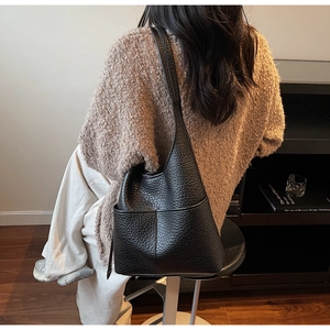 Side view of black lychee grain leather bucket bag worn by model in minimalist setting