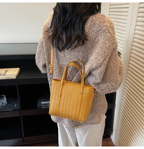Detail of yellow woven leather tote bag featuring rich texture and silver metal hardware