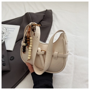 Detail of cream white half-moon bag with decorative wooden beads and buckled leather strap
