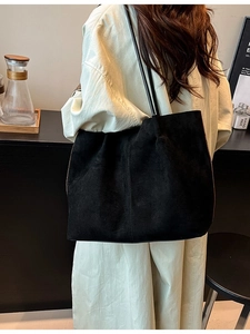 Large black suede tote bag with slim shoulder straps worn by model in minimalist setting