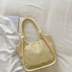 Close-up of pale yellow woven tote bag showing detailed leather texture and soft strap