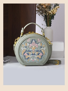 Close-up of sage green round crossbody bag with traditional floral embroidery and gold hardware