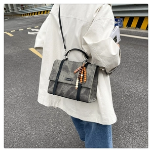 Détail d'un sac bandoulière gris vintage avec pompon en bois et texture brossée