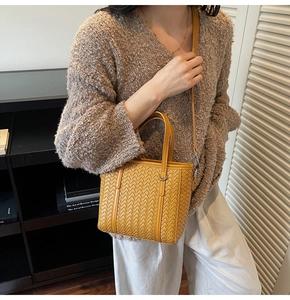 Detail view of woven ginger yellow handbag with leather texture and silver buckles