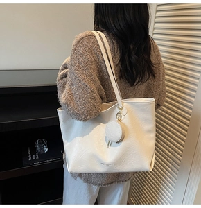 Detail of white faux leather tote bag with circular pendant pouch on shoulder