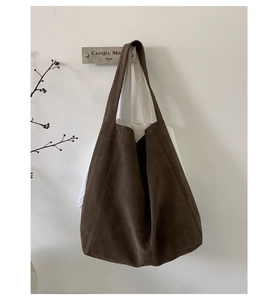 Detailed view of the dark brown suede tote bag hanging on a minimalist white wall
