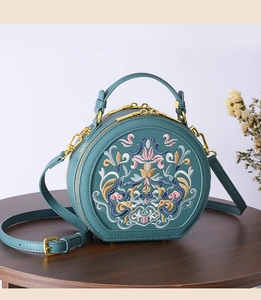 Detail of teal semi-circle bag featuring colorful floral embroidery and gold hardware