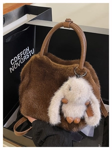 Details einer dunkelbraunen Kunstfelltasche mit weißem Plüschhasen-Anhänger und Griffen