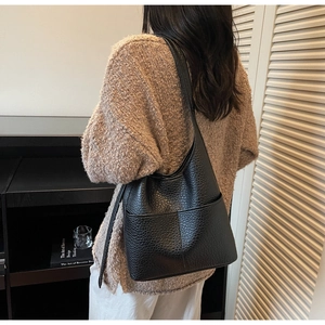 Detail of black pebbled leather tote bag showing fine texture and shoulder strap on model