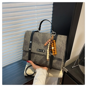 Détail du sac à main gris foncé texturé avec poignées en cuir et breloque en perles de bois