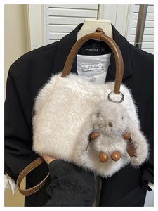 Detail einer weißen Plüschhandtasche mit braunen Ledergriffen und Hasenanhänger