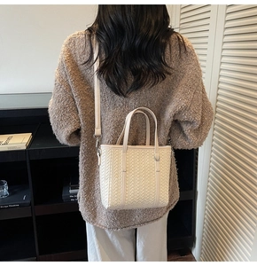 Detail of cream woven bucket bag showing the texture, top handles and shoulder strap