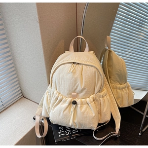 Detail of quilted beige nylon backpack showing large drawstring pocket and padded texture