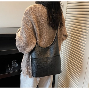 Detail of black pebbled leather bucket bag with double exterior pockets shown on shoulder