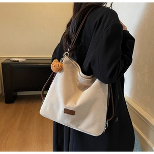 Seitenansicht einer großen beige Canvas-Tasche mit braunen Riemen und Plüschbär-Anhänger