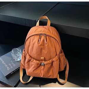 Detail of burnt orange water-repellent nylon backpack with drawstring pocket on dark wood