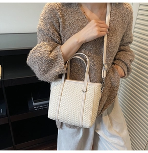 Detailed texture of the woven cream bucket bag with adjustable shoulder strap and hardware