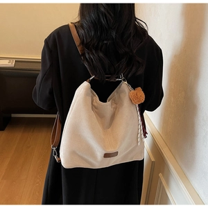 Detailansicht der cremefarbenen Hobo-Bag mit braunem Lederriemen, Plüsch-Anhänger und Band