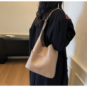 Detailed side view of beige pebble grain leather bucket bag with two front pockets