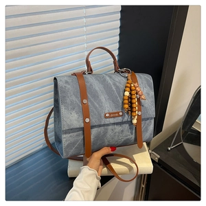 Détail d'un sac en toile bleu denim avec lanières en cuir, rivets et charm en perles